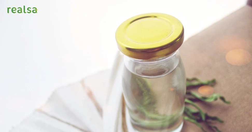 A clear glass bottle filled with Virgin Coconut Oil placed on a neutral surface, styled with natural elements to highlight VCO purity and freshness