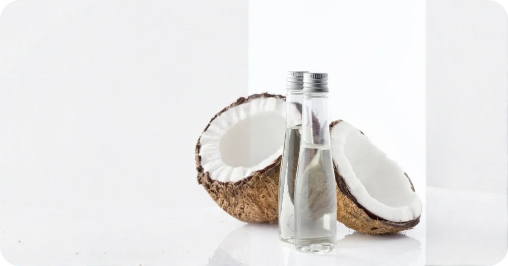 Premium VCO Product Display - Realsa Indonesia High-quality Virgin Coconut Oil in slim glass bottles with fresh coconut halves, supplied by Realsa, a leading Virgin Coconut Oil Exporter Indonesia.