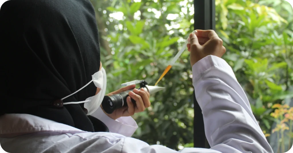 A quality control technician employed by Indonesian exporters using a refractometer to measure the Brix level of coconut sap.
