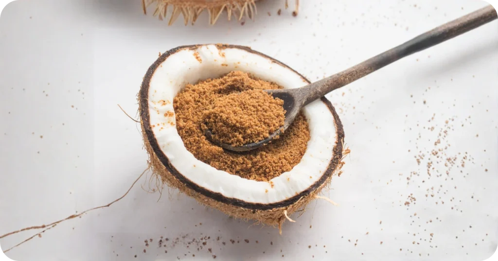 Granular natural coconut sugar presented inside a split white coconut, highlighting the unrefined quality for food manufacturing.