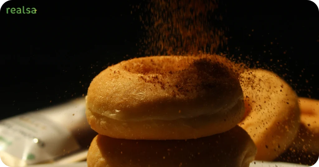 Close-up of golden-brown natural sugar dusting falling onto a stack of donuts, highlighting the texture of unrefined sweeteners.