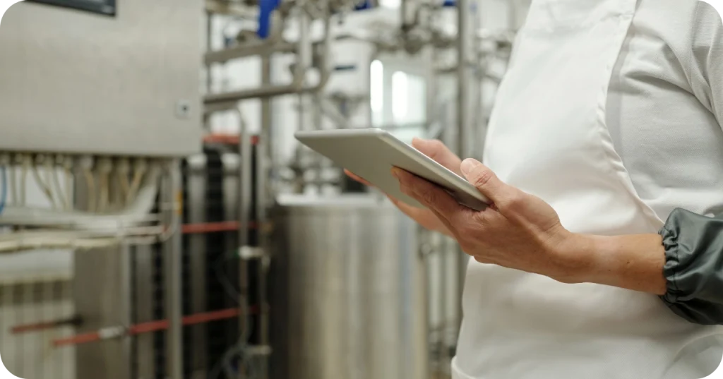Modern Sugar Quality Control Factory worker in a white apron conducting a digital inspection of stainless steel machinery used for export-grade sugar manufacturing.
