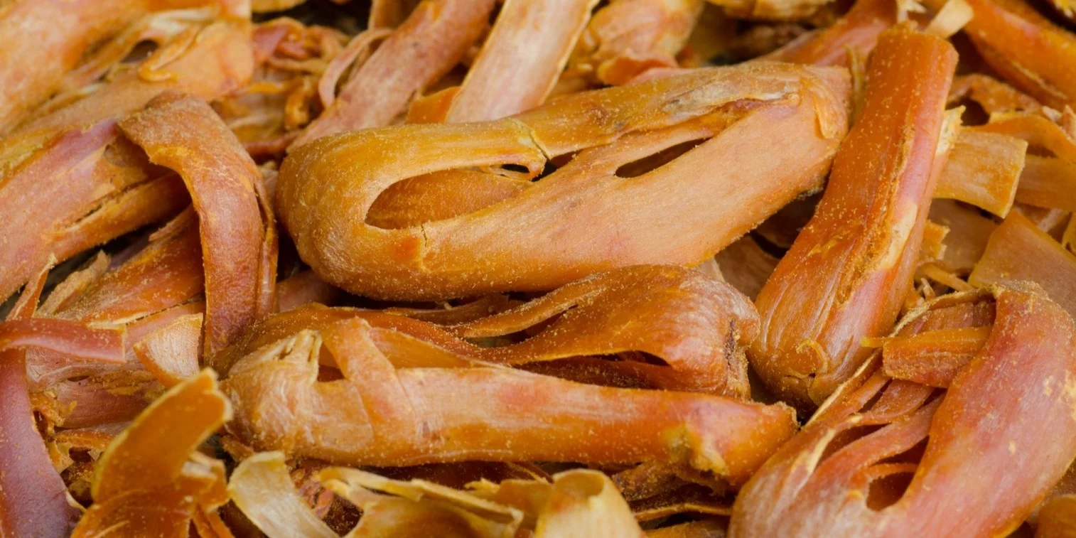 A macro close-up photograph capturing a dense pile of textured, dried whole mace arils. The characteristic curved, holed, reddish-orange blades of the spice fill the entire frame, showing their unique shapes.