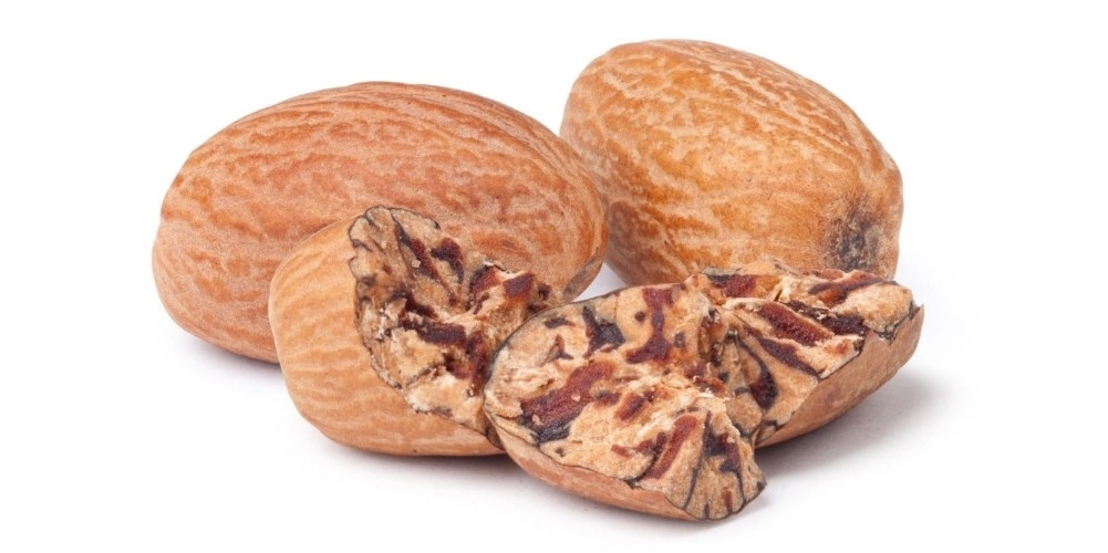 A detailed close-up of premium cracked and broken nutmeg seeds, showing the dark textured outer shells and the rich, patterned interior of the spice.